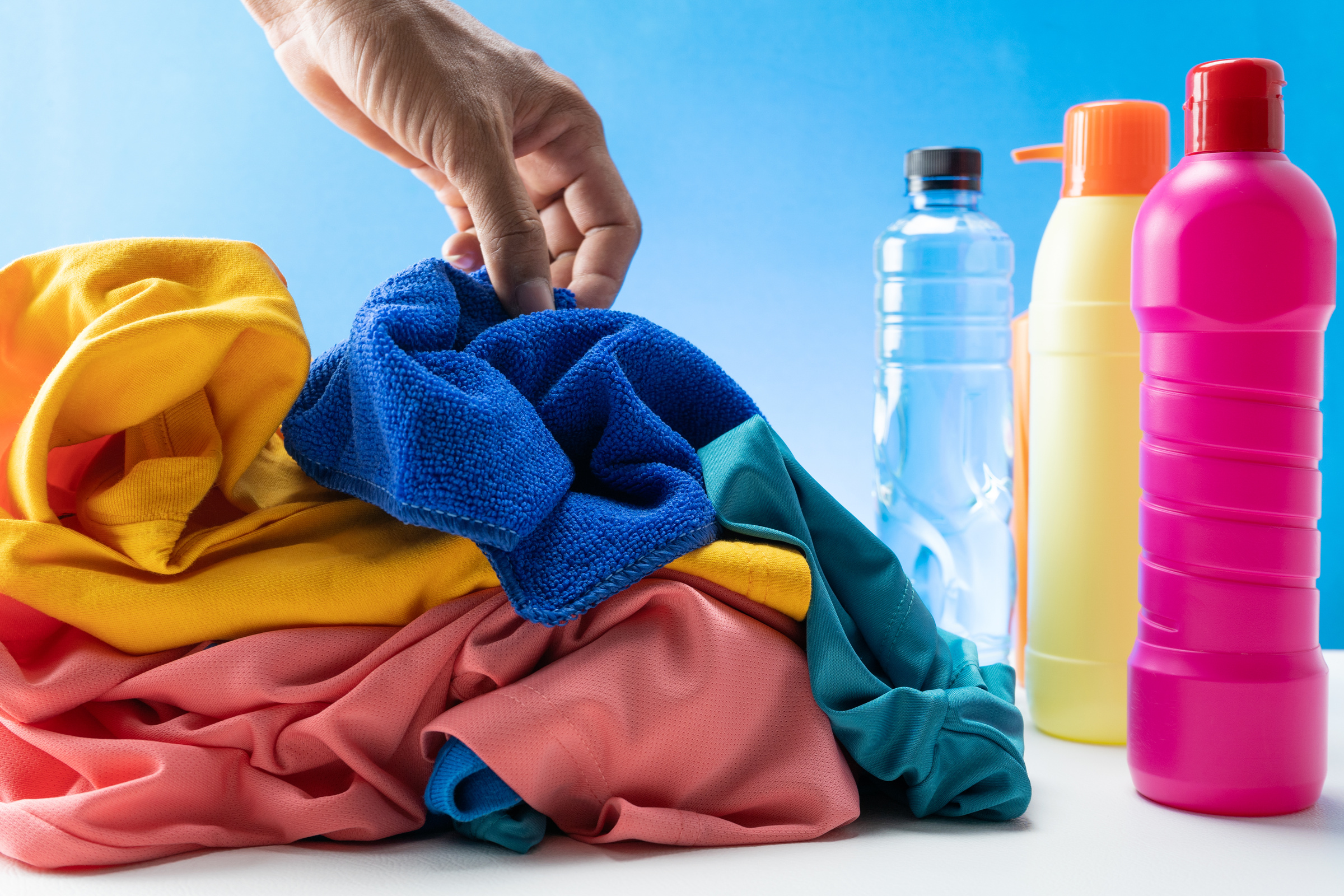 Hand Picking Pile Colorful Clothes Near Bottles of Cleaning Products